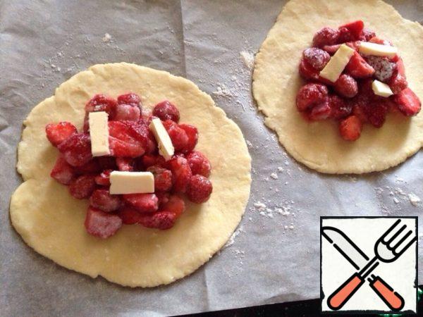 Get the dough out of the fridge. Divide into 3-4 parts and roll out each piece to a thickness of 0.5-0.7 cm and Then carefully transfer to a baking tray lined with parchment paper. In the center of each biscuits put strawberries, and on top of 2-3 small pieces of oil.