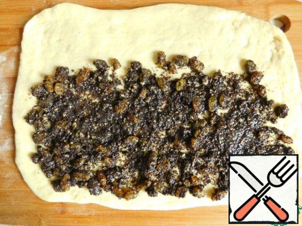 Divide the finished dough into two equal parts. We cover one part again, and roll out the second part of the dough (not very thinly) into a rectangle. Put half of the filling on the dough, distribute evenly, not reaching the edge on one side of the rectangle.
