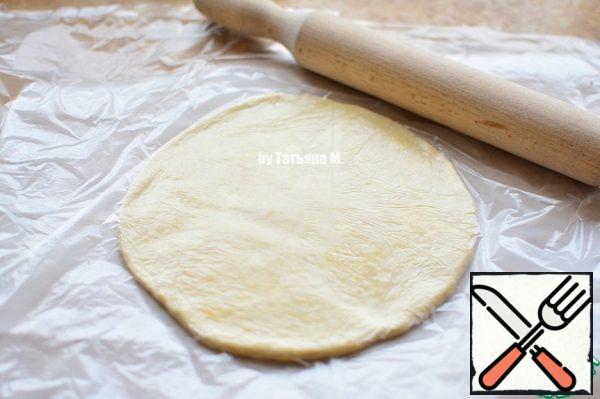 Prepare 2 sheets of parchment;
On one of the sheets to spread the ball of dough, cover with a food package and roll out into a circle;