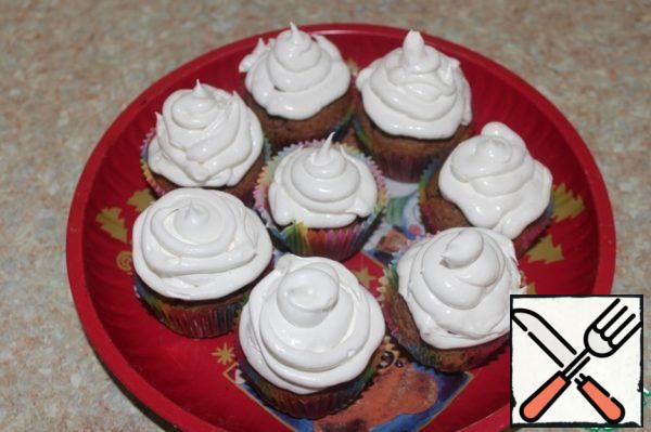 With a pastry bag with a round nozzle decorate muffins cream.