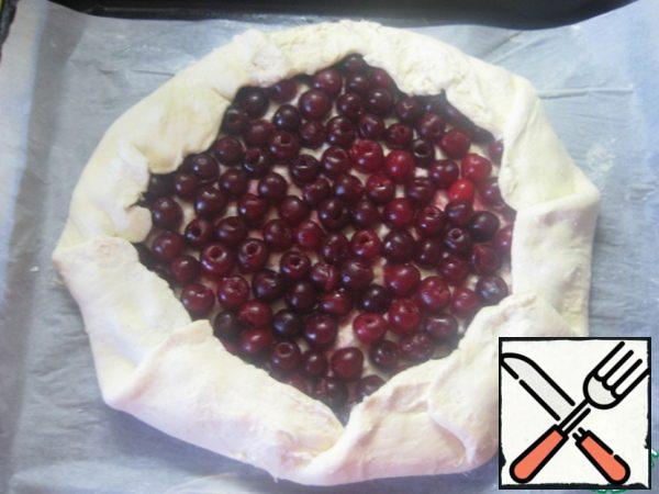 On top of the curd filling, put the cherries. Wrap the edges on top of the filling. The edges of the cake and cherry sprinkle with sugar.
Carefully move the sheet of parchment with a biscuit on a baking sheet.
Bake in a preheated 200 degree oven for 20-25 minutes until Golden brown.