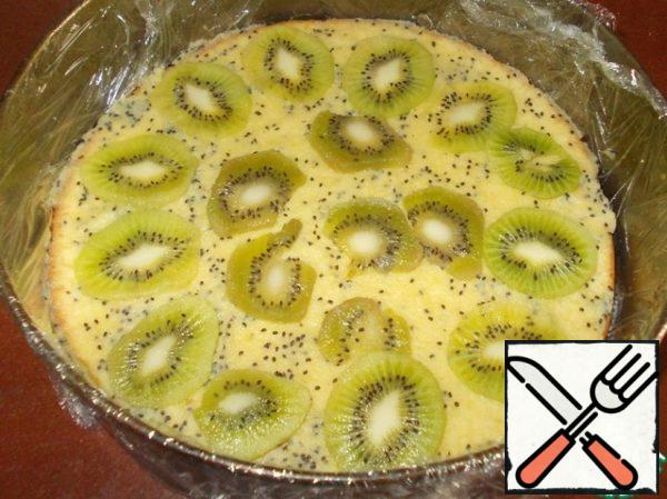 In the form put one of the cakes. Grease it with half mashed kiwi fruit and lay out the kiwi slices.