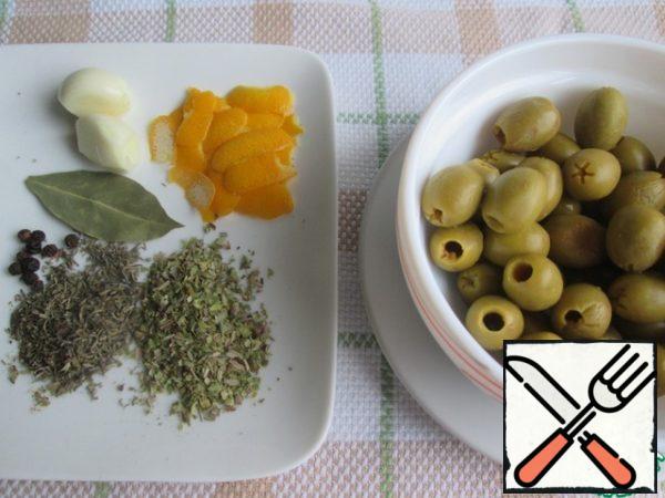 Remove the olives from the jar, let the liquid drain.
Remove the zest from the lemon with a vegetable peeler, cut into wide strips.
Prepare dried herbs, bay leaf, black pepper and garlic.