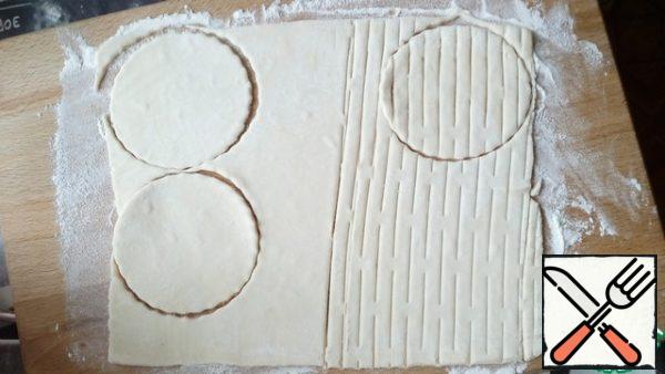 Roll out the dough and cut out 4 cups with a round notch.
In the second half of the dough, go through the roller for cutting the cubes, cut out 4 more mugs. If there is no roller, you can make several parallel incisions with a knife on the cut circle without reaching the edges of the dough.