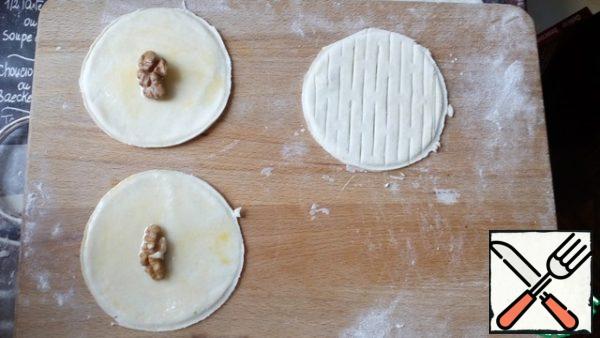 Grease the dough with yolk for 4 circles, sprinkle with powdered sugar. Put half or a quarter of the nut.
