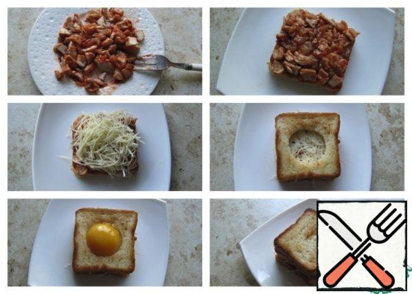 If the fillet is large, the cooled pieces of meat should be disassembled with a fork into fibers. Place the chopped chicken fillet with ketchup on a slice of toast. Put a layer of grated hard cheese on top. Cover the top with a slice of bread, in which pre-cut a glass hole in the center. Pour the yolk into the cut-out hole. Cover the top with a slice of bread.

