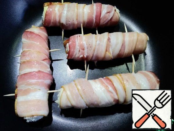 Roll wrapped with a ribbon of bacon. The beginning and the end fastened with toothpicks or skewers. Heat a little vegetable oil in a pan and fry the rolls on all sides.