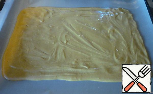 The resulting viscous batter is quite thick. Half of the dough smeared on a greased baking sheet. It is better to put baking paper or non-stick Mat. It is more convenient to do it with wet hands.