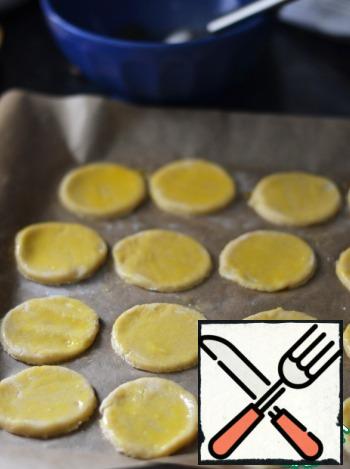 Cookies spread on a baking sheet, lined with baking paper. Brush them with egg yolk.