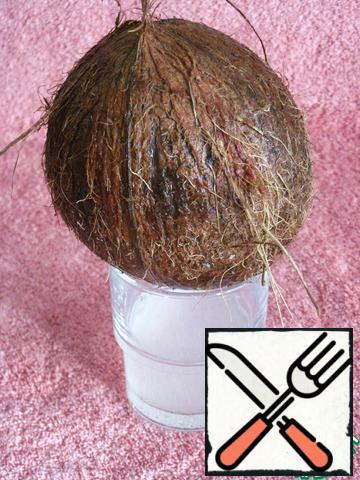 This recipe uses only coconut flesh. To get it, wash and dry the nut. Make a hole in the top of the coconut and extract the milk. It is not used in the recipe. You can just drink it, as the liquid contains many useful substances. Or use it in another recipe.
