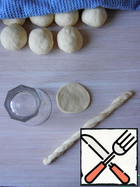 Cover the dough pieces with a film and leave for proofing for 10-15 minutes. After that, roll out the bun in a round layer and cut out a glass of cake. The remaining edges are stretched into a long rope and twisted into flagella