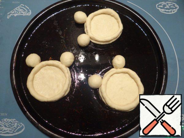 Collect cheese cakes immediately on a baking sheet, greased with vegetable oil (I baked cheese cakes on two trays, because I have a small oven). First, I put the circle, then apply the ears to the Cup, the ends of the" rim " connect, put on a circle of dough.
