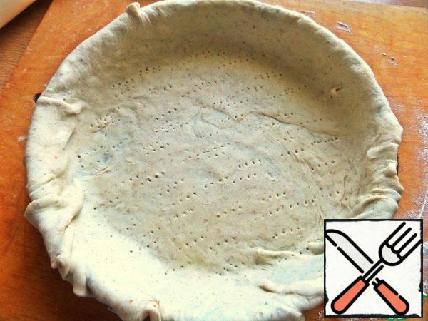 Wrap the layer on a rolling pin and transfer it to a greased Teflon mold with a diameter of 26 cm, roll up the edges on the sides.
Prick the bottom with a fork.
