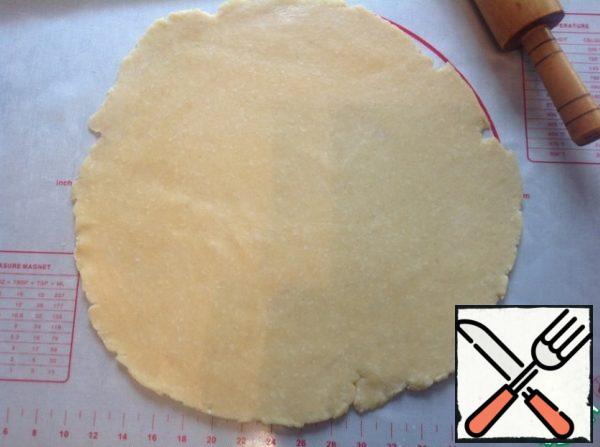 The cooled dough is rolled out on a lightly floured surface into a circle with a diameter of 35-40 cm .
Transfer to a baking sheet lined with parchment.
To prevent the cake from tearing, I roll it out on a large silicone mat, then spread it on top of a baking sheet covered with parchment, and turn it over with a silicone mat.
