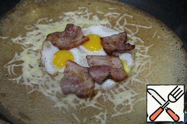 Fry the pancake on one side, turn it over and sprinkle some cheese. From above to lay eggs on which to place the slices of ham.