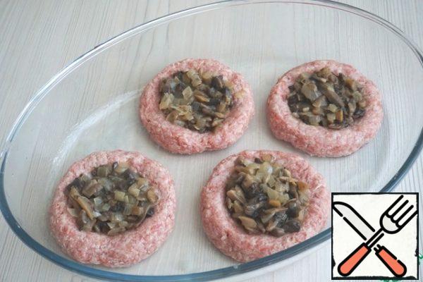From the total amount of minced meat, form tortillas of the same size. Put the cakes in the baking dish, make a recess, you can use the bottom of a glass or a spoon. Put the mushroom filling in the middle, smooth it out.
