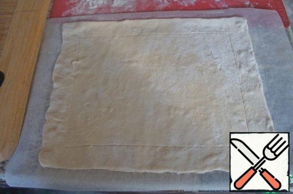 Prepare the products. The dough in advance, remove from the freezer so it could thaw. Turn on the oven at 200 * C. Roll out the dough into a rectangle the thickness of a coin. Outline the rim, stepping back from the edges about 2 cm.