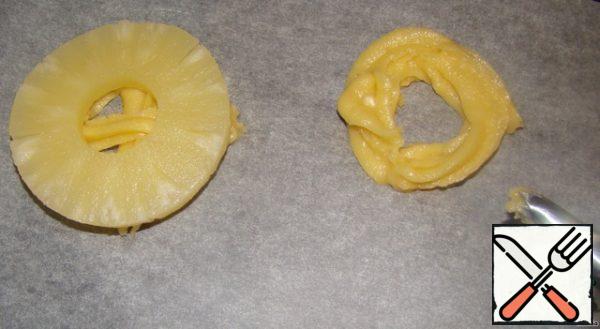 Cover the baking sheet with baking paper. The dough is spread in a pastry syringe or bag. And with circular movements we squeeze out the base for cakes on paper. Put a piece of pineapple on top, lightly press the dough under the pineapple, it should protrude from under the pineapple.
