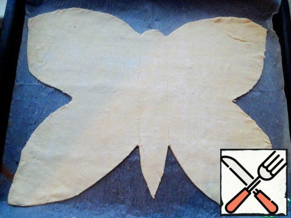 Half of the puff pastry roll out into a thin layer. Put it on baking paper in a baking sheet. Trim the edges of the dough in the shape of butterfly wings.