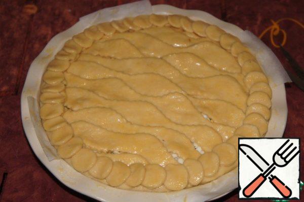 Roll out the second part of the dough thinly, cut into strips simulating waves, and put on the filling. Leave a few small gaps between the strips for steam to escape. Fold the edges of the bottom cake over the cake and lubricate with egg.
From the remaining dough, cut out small circles and put them on the edge of the pie, imitating scales.
Grease the top of the cake with beaten egg and put it in the oven, preheated to 220 * C.