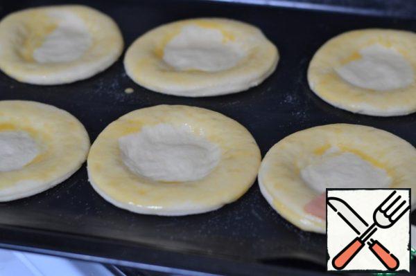 Transfer circles to prepared baking sheet.
With your fingers make an indentation in the middle for the filling.
Just squeeze the dough. Let's leave it for 10 minutes.
Circle cheese cake put some beaten egg.