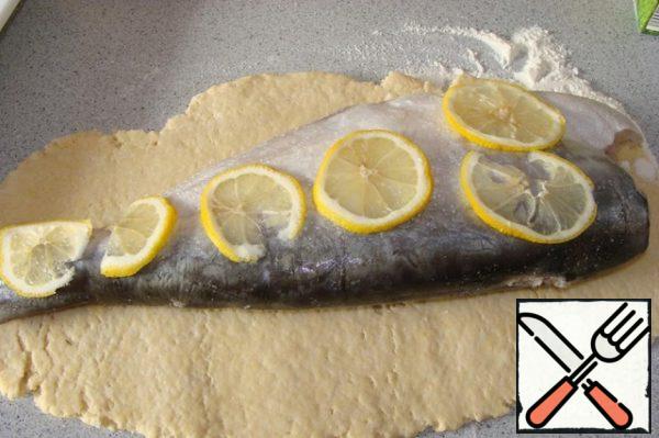 Roll out the dough, put the fish on the fish - sliced lemon.
