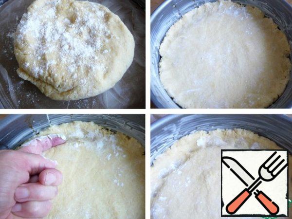 In the dough add a little flour, gather in someone. The dough is soft.
To move to the form.
Propylite hands with flour, flatten the dough.
Index finger, covered with flour, press the dough along the edge of the form, so it's a little up in the air.