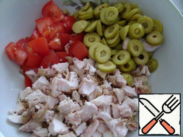 Cut the tomato into cubes, the olives into rings, and the chicken into small pieces.

