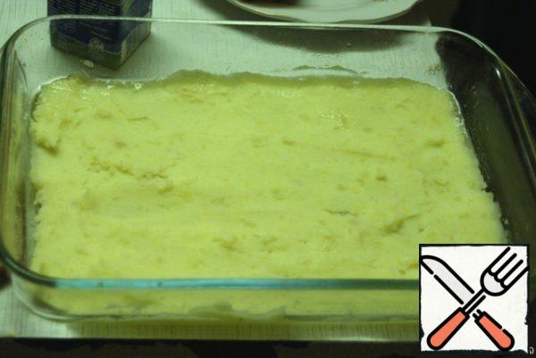From pre-cooked potatoes make mashed potatoes (add milk and butter).
Baking grease with vegetable oil, then spread half of the puree. This will be the first layer.