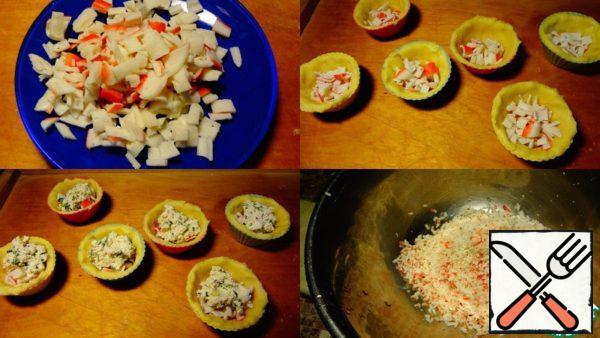 Half of the crab sticks need to be coarsely chopped and put into each mold together with the dough.
Put 1 tablespoon of feta cheese in each mold.
Sprinkle grated hard cheese on top.