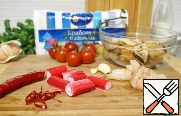 Meanwhile, prepare the filling. Shrimps are cleaned from the shell and intestinal vein. Cut all seafood and crab sticks into large pieces. Chop the chili pepper into thin rings, chop the garlic.
