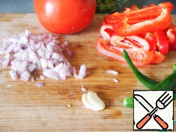 Prepare the vegetables: traditionally used bell peppers - cut into strips; onions - chop; green peas or string beans - defrost; tomatoes - scald, peel and finely chop, and later just rub the tomato whole through a sieve; I also prefer to use garlic - crush with a knife, and hot chili pepper - cut in half to give the aroma of oil.
