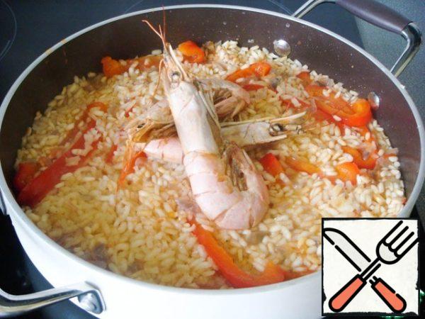 Due to uniform heating, the rice should reach readiness in about 20 minutes. A couple of minutes before that, seafood and other products that require minimal cooking time are laid out on rice. Starting with those that need more time. I have large shrimp first.