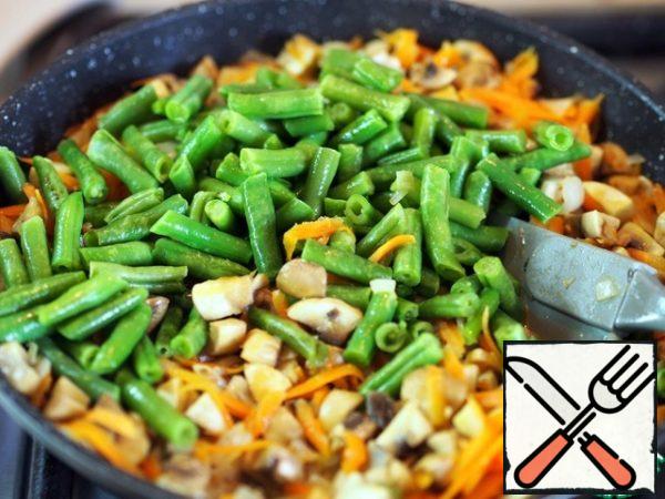 Heat a frying pan with vegetable oil, crush a clove of garlic and fry it for 1-2 minutes, then discard.
Put onions, carrots, mushrooms, and beans in a frying pan with an interval of 2-3 minutes for frying. If the beans are frozen, defrost them first.