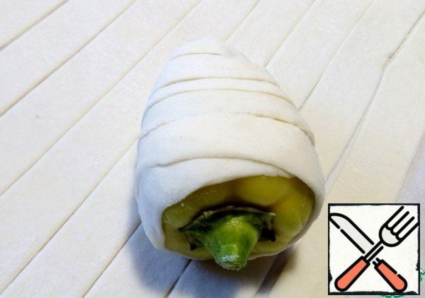 Roll out the puff pastry to a length of 2-3 mm thick, cut into strips 2-2.5 cm wide and start wrapping the peppers with the wide side overlapping, in a spiral. At the end, roll the dough well. If the strip is missing, add the next one. While rolling out, lightly brush the dough with beaten egg in some places so that it sticks well.
