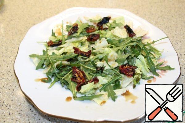 On a platter, put the coarsely torn iceberg lettuce and arugula leaves, dried tomatoes, sprinkle with a small amount of dressing.
