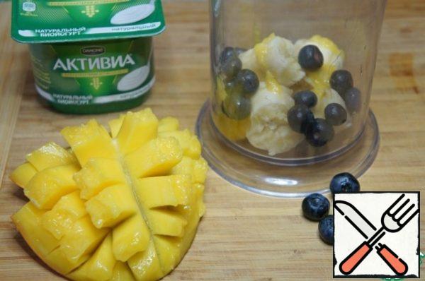 Break the banana into pieces and put it in the bowl of a blender. Add blueberries.
