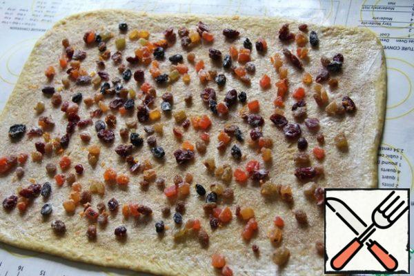 Divide the finished dough into 4 parts. Roll out one piece into a rectangle about 20x35 cm in size. Grease the dough with a fourth part of butter, sprinkle with a fourth part of sugar with cinnamon and spread a fourth part of candied fruits on the surface. Roll out lightly with a rolling pin.
Roll the roll with a short edge.

