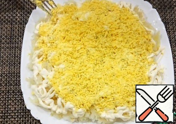 Then grate the egg yolk on a fine grater and spread it well with a fork over the entire surface of the salad.
