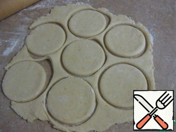 Sprinkle the table very lightly with flour, roll out the dough into a circle not very thin, about 0.3-0.4 cm, cut out circles with a diameter of 8-9 cm.
