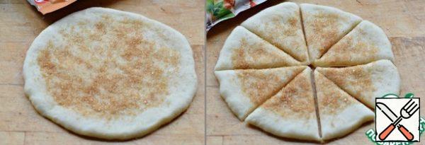 Roll out each blank into a round cake with a thickness of 0.4-0.5 cm.
Evenly sprinkle the surface of the cake with sugar and cinnamon (about 0.5 tsp, more or less, a matter of taste), retreating from the edges by 1 cm. I use sugar with cinnamon.
Cut the pie into eight equal parts.
