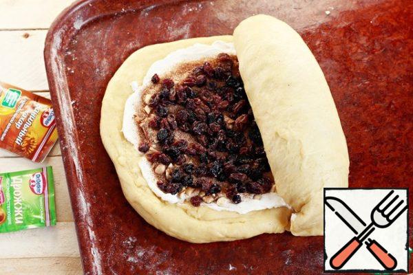 Spread the dried raisins evenly, lightly press the filling with the palm of your hand. Roll the workpiece into a roll, immediately wrap the ends. Gently pinch the edges, and wrap the ends in a roll.
