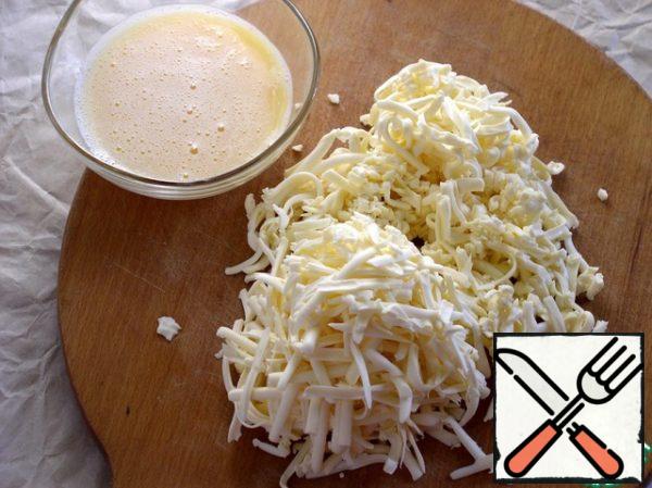 Divide the dough into two parts.
Grate the cheese on a coarse grater.
Beat the eggs into a cup and lightly beat with a fork.
