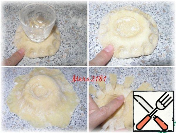 Form a ball from each piece and press it slightly to make a high bun. Then, using a convenient container (I used a glass with a flat bottom), make a recess in the center. And I press the edge of the dough with my index finger and do it in a circle. Using a rolling pin, lengthen the edge of the bun. Use scissors to make incisions before the thick base begins. Then I bend the resulting strips through one into the center of the recess and press.
