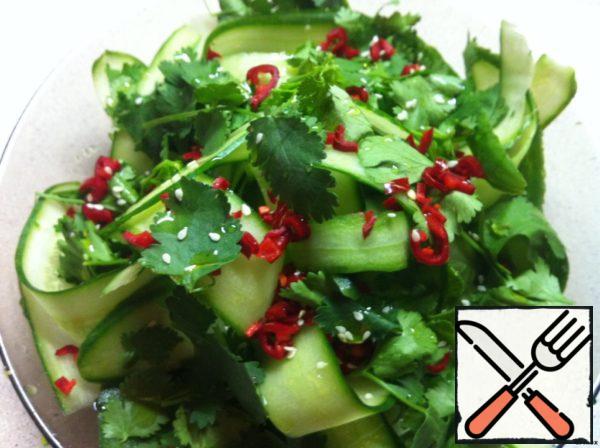 Using the slider, cut cucumbers into long thin strips on a plate with dressing, cut into bones (they give too much moisture) from four sides. Then add the cooked cilantro leaves, chili pepper and sprinkle with sesame seeds.