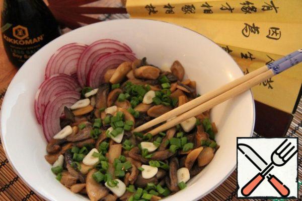 Peel the onion, wash it, cut it into slices. Wash the green onions, chop them finely. Peel the garlic, wash it, cut it into slices. Arrange the mushrooms on plates, sprinkle with garlic and green onions