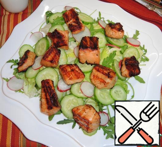 On a serving plate put a salad mix, fresh cucumber and radish, cut into thin circles. Put the fish on top. Sprinkle the salad with olive oil, lightly sprinkle ground black pepper and sesame seeds and serve.
