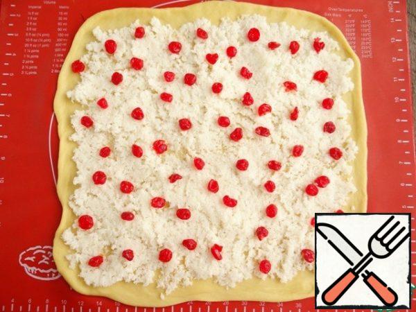 Spread 1/2 part of the filling on the dough, distribute it, sprinkle 1/2 part of the dried cherries.

