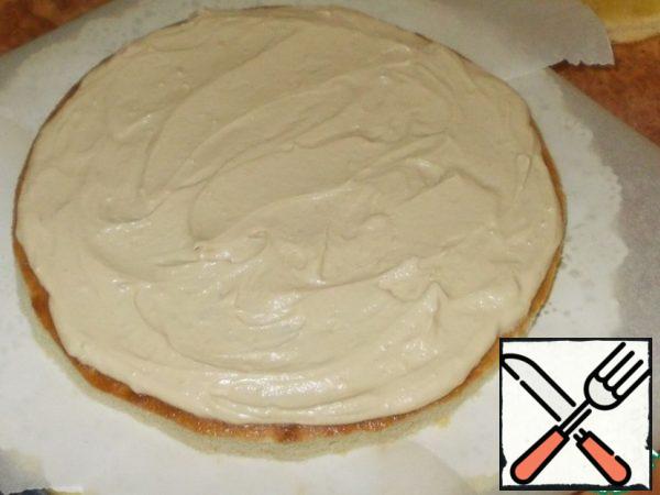 Spread the first cake. Carefully place the strips of parchment under the cake so that the cake does not stain the napkin during the assembly process. Of the total amount of cream, put one spoonful into a pastry bag, and visually divide the rest of the cream mass into three parts and spread one third on the first cake. Distribute evenly.
