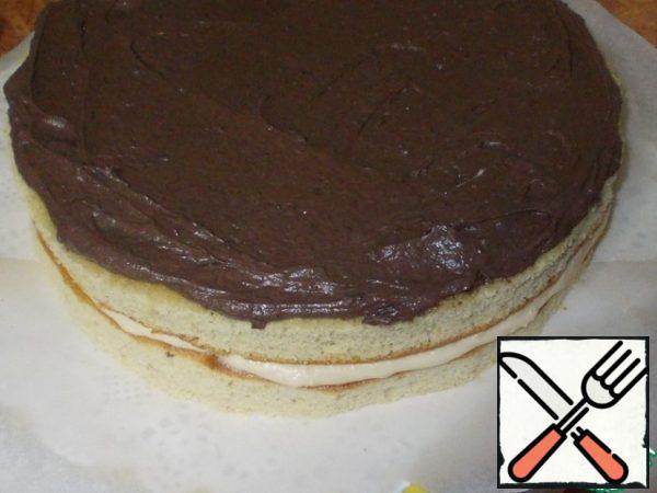 On top of the first cake, smeared with a light cream, lay out the second cake and smear it with chocolate cream. It takes half of the remaining cream to coat the second cake.
